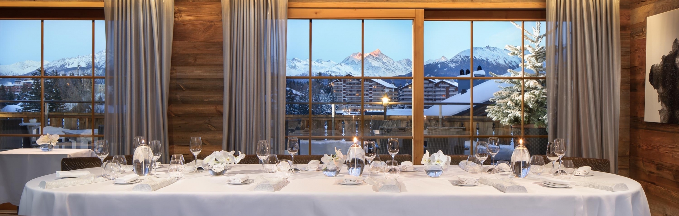 Table élégamment dressée dans une salle de restaurant avec vue sur les paysages enneigés de Crans-Montana.