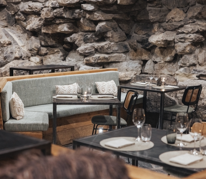 Salle du Bistrot des Ours à Crans-Montana, avec tables dressées, banquettes et murs en pierre naturelle.